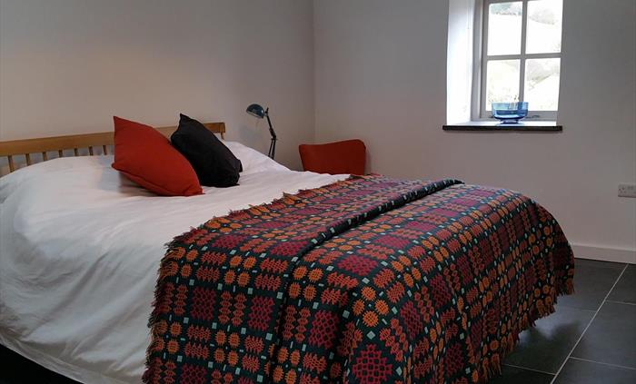Super king sized bed with crisp white bed linen and a traditional Welsh blanket in warm dark colours of deep red, orange and teal.